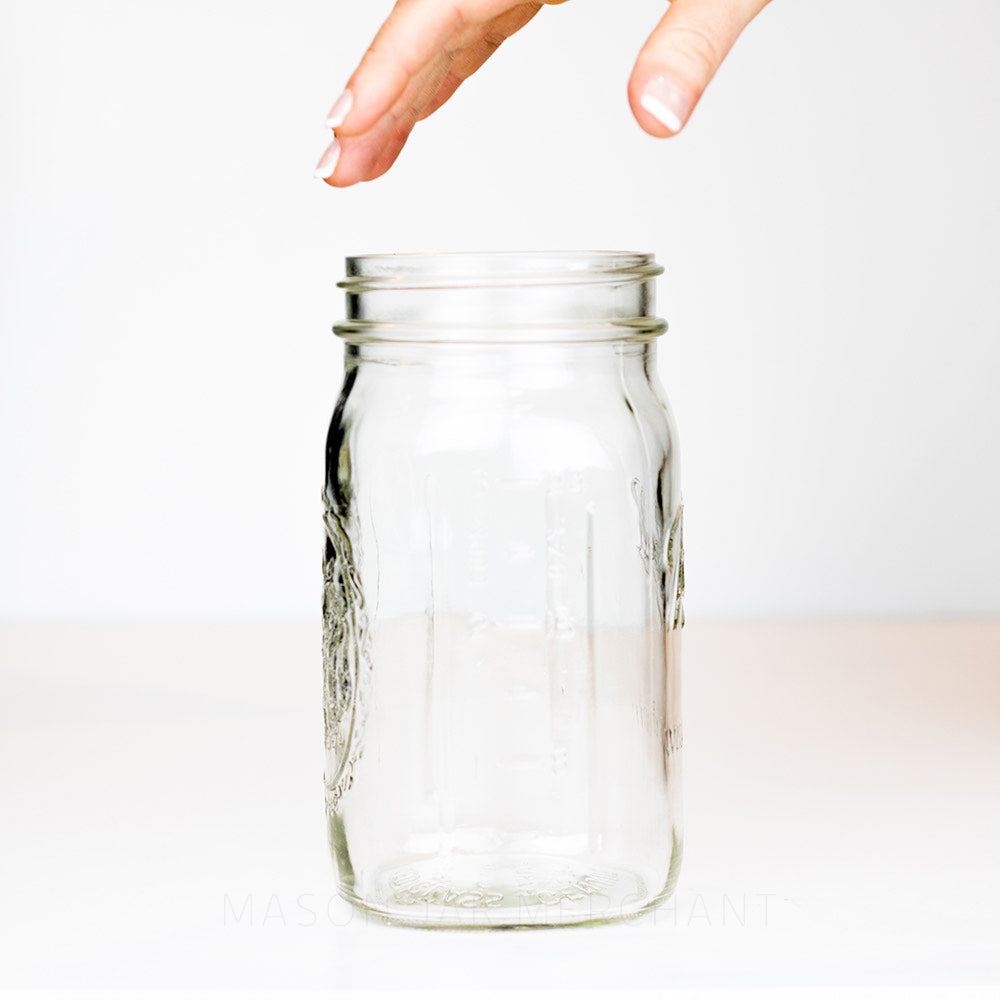 A hand about to pick up a Wide mouth quart mason jar with Ball logo, against a white background