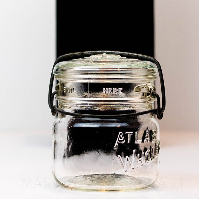 A close up of a Vintage 1940s Atlas Wholefruit wide mouth wire bail mason jar with Atlas whole fruit jar engraved in it against a white background