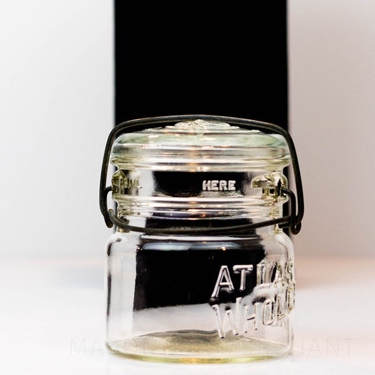 A close up of a Vintage Atlas Wholefruit wide mouth wire bail mason jar against a white background