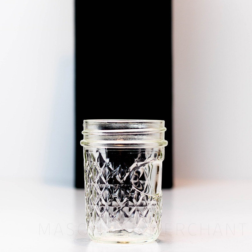 A clear close up of the details of a Regular mouth half pint mason jar with a quilted pattern and space to add a label, against a white background