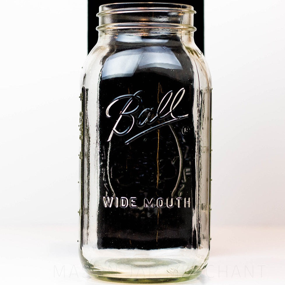 A close up of a Wide mouth half-gallon mason jar with Ball Wide mouth logo, and fruity oval design visible on the back side of the jar. against a white background