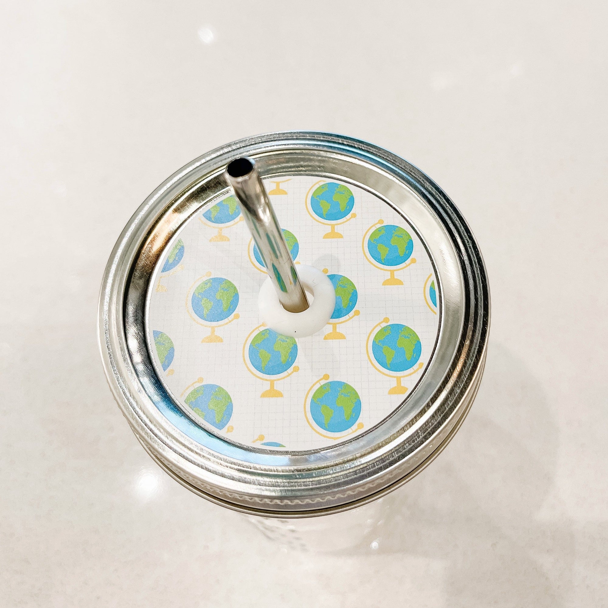 Silver lid with a globes on graph paper patterned mason jar straw lid against a white background.