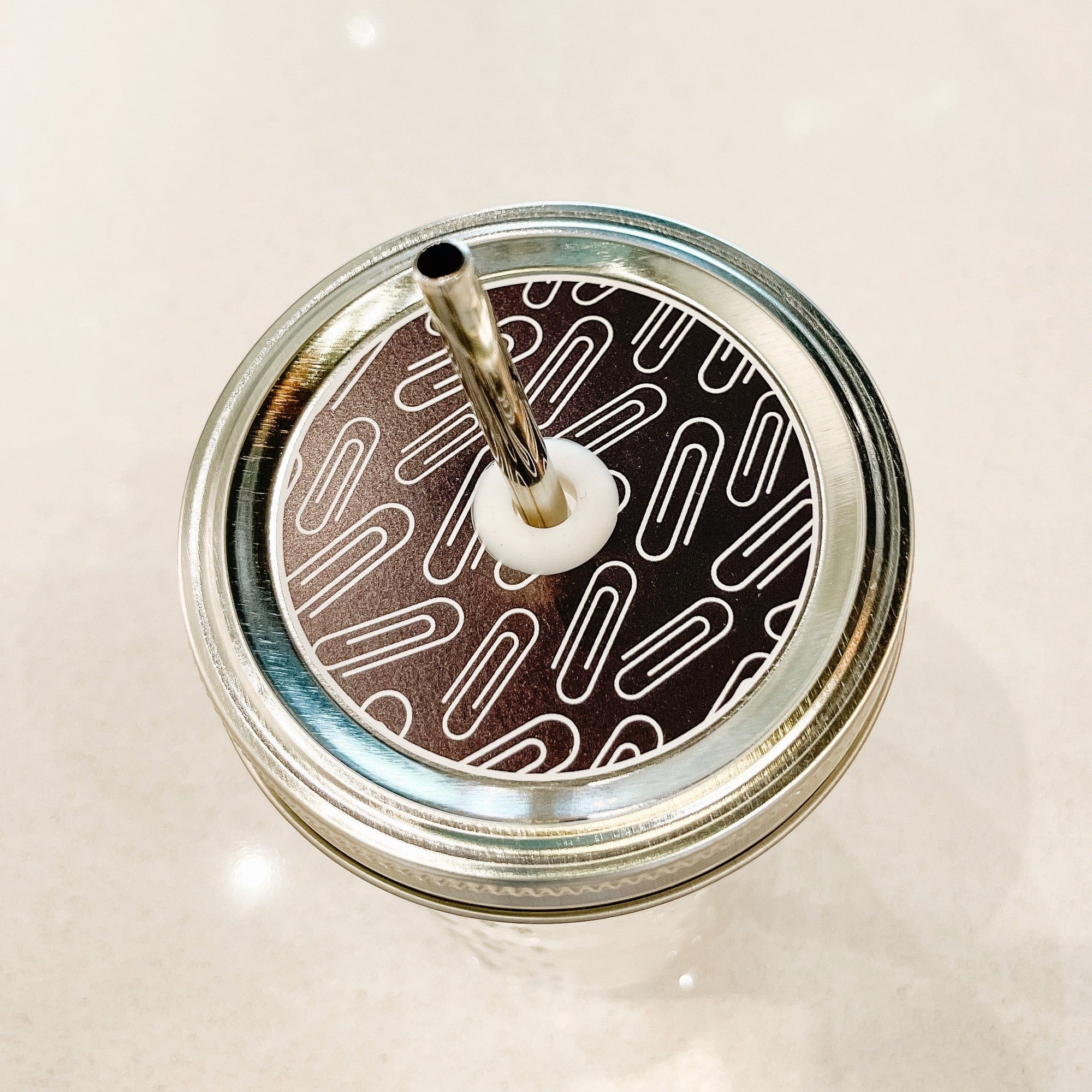 top photo of mason jar lid with paper clips on a black background