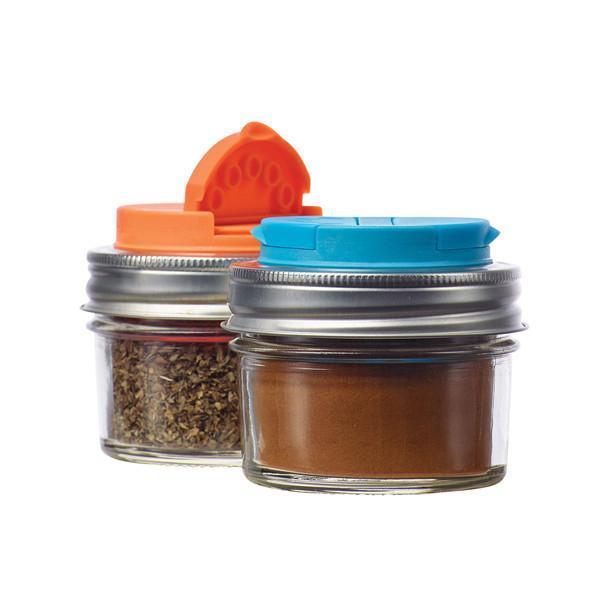 Orange and black mason jar spice/ shaker lid on top of a reusable mason jar on a white background. It has spices and herbs inside.