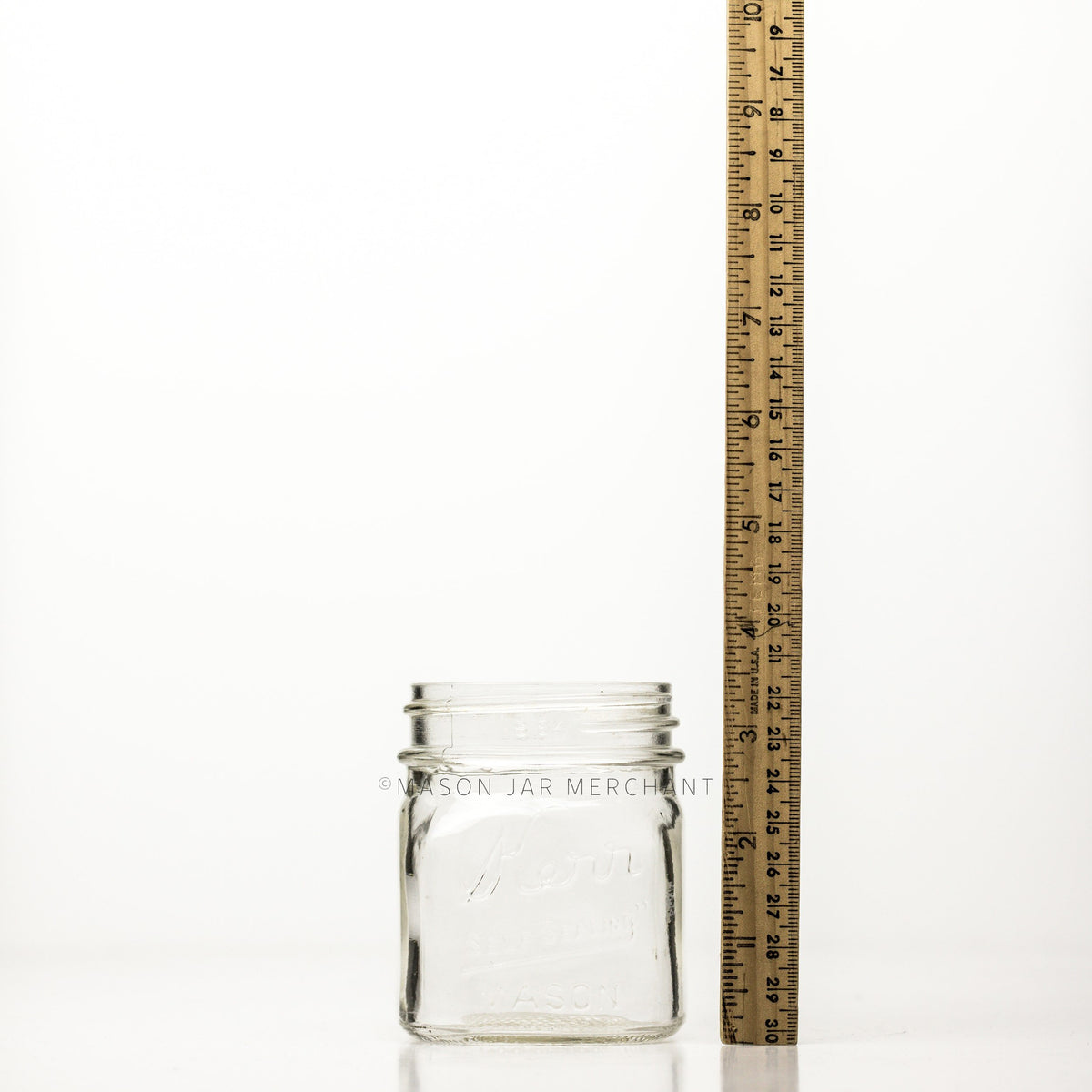 Regular mouth half-pint mason jar with square sides and Kerr self-sealing logo with a meter stick beside it against a white background 