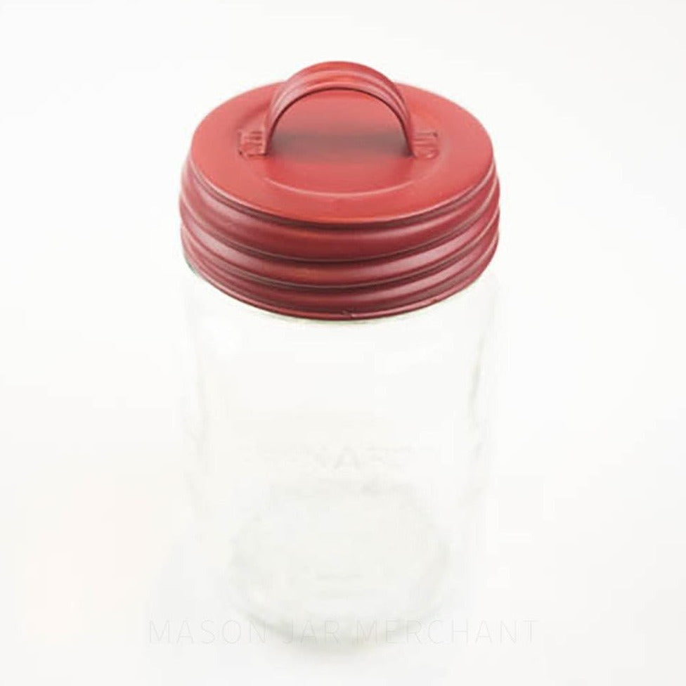 Close-up of a matte red lid with a handle on a regular mouth mason jar against a white background 