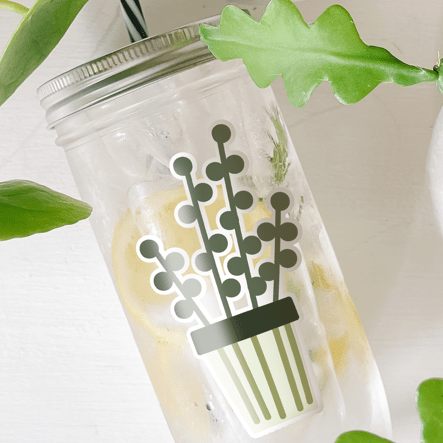 Tumbler with water inside and a sticker of a potted plant printed on it. Photographed as a flat lay in a white background and some potted plants.
