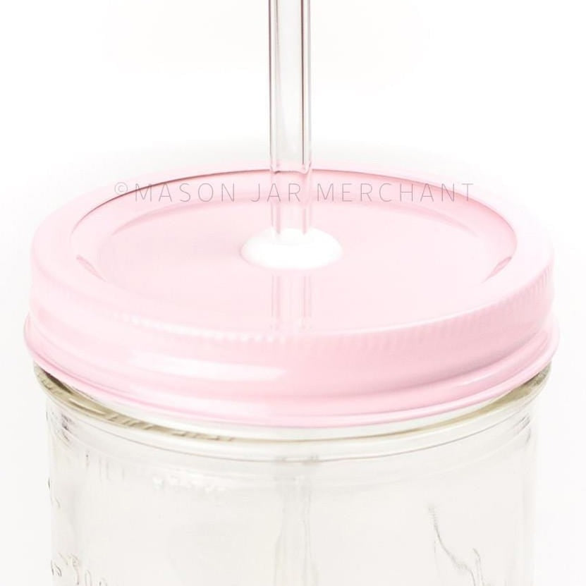 Close-up of a 24 oz wide mouth mason jar with a pastel pink custom painted lid with a white silicone grommet and a glass straw, against a white background