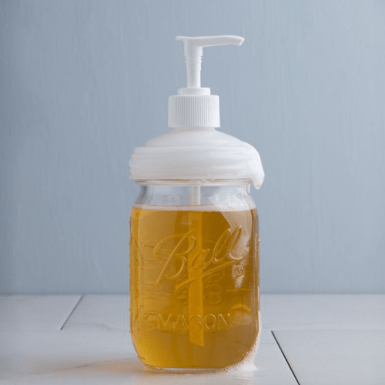 a white reCap mason jar pump lid on a regular mouth jar with orange soap inside. It sits on a bathroom counter on a blue background