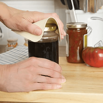 A person using a beige mason jar opener to open a jar of jam on a kitchen counter