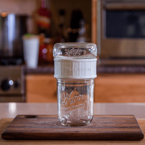 a to go jar with a spill proof white wide mouth lid sits on a cutting board on a kitchen counter