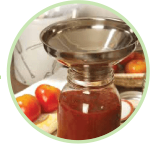 stainless steel funnel on top of a glass mason jar filled with tomato sauce and is shown on top of a counter, It has tomatoes beside it