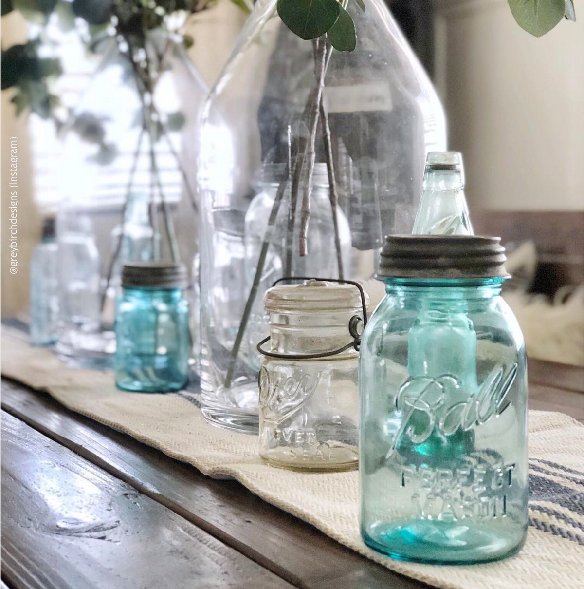 A variety of mason jars on a table, including a blue Ball mason jar with a zinc lid in the foreground