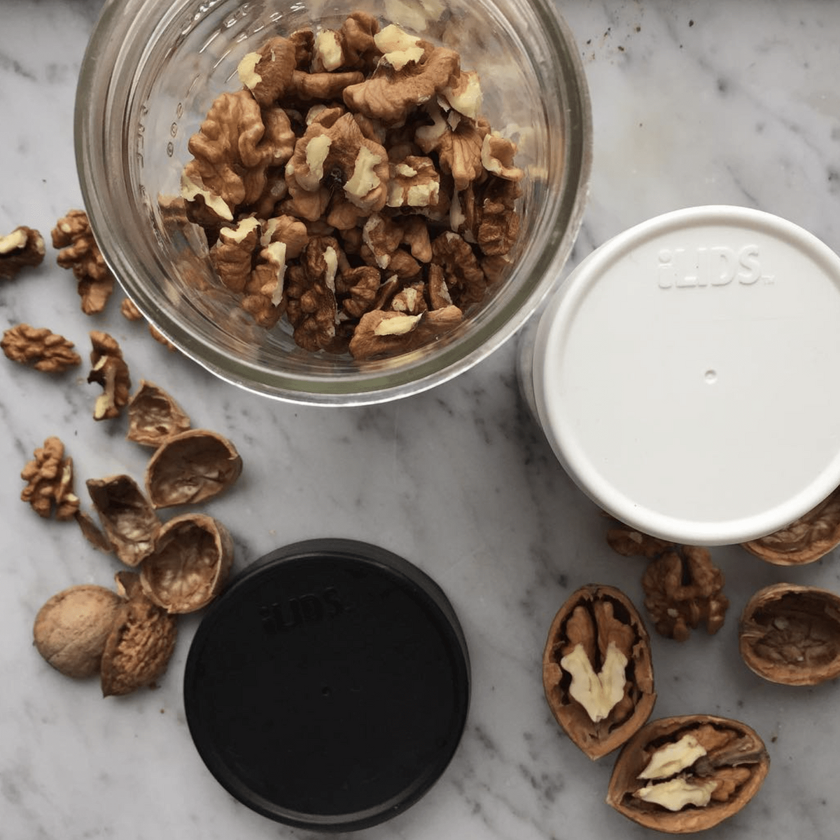 black and white storage lids sit on a counter with a glass jar full of nuts