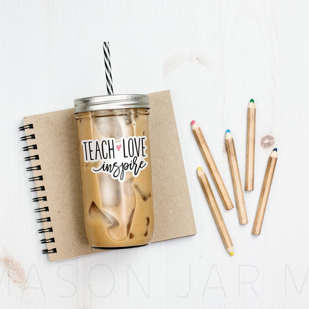 Tumbler with iced coffee and print that says "Tech Love Inspire" with a heart design in text. Photographed against a neutral colored notebook and some color pencils.