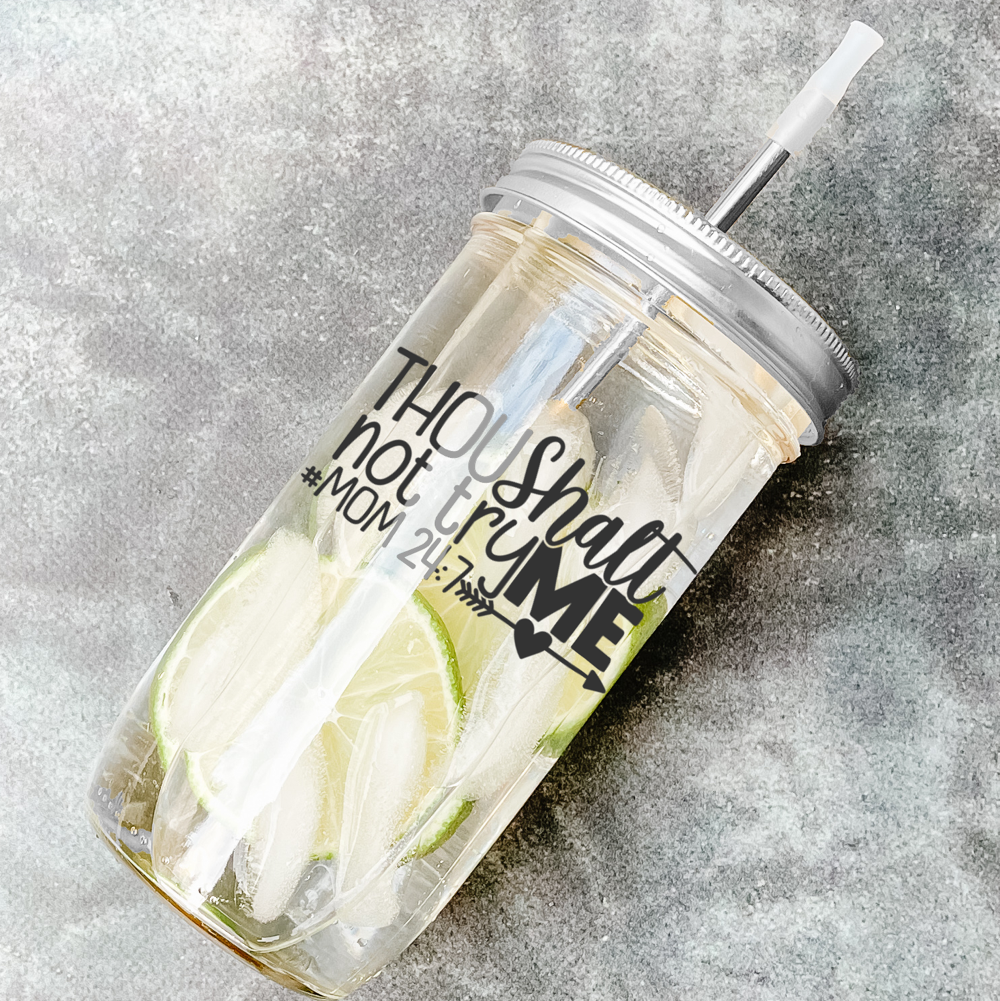 Mason jar tumbler filled with a citrus water drink and has a silver lid and straw and a calligraphy print that reads "Thou Shalt Not Try Me #Mom 24:7." Photographed against a marble countertop.