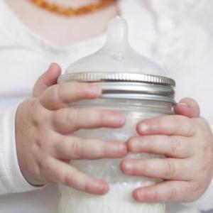 close up of baby holding a half pint glass reusable mason jar with silver ring and rubber bottle lid