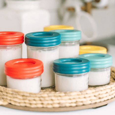 Mason jar bottles storing milk in 8 oz and 4 oz with Paprika, Mango, Aqua, and Ocean plastic lids all inside a native tray.
