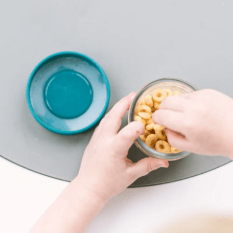 A child grabbing snacks inside an open 4oz mason jar bottle with Ocean colored lid set against a white countertop with a gray placemat.