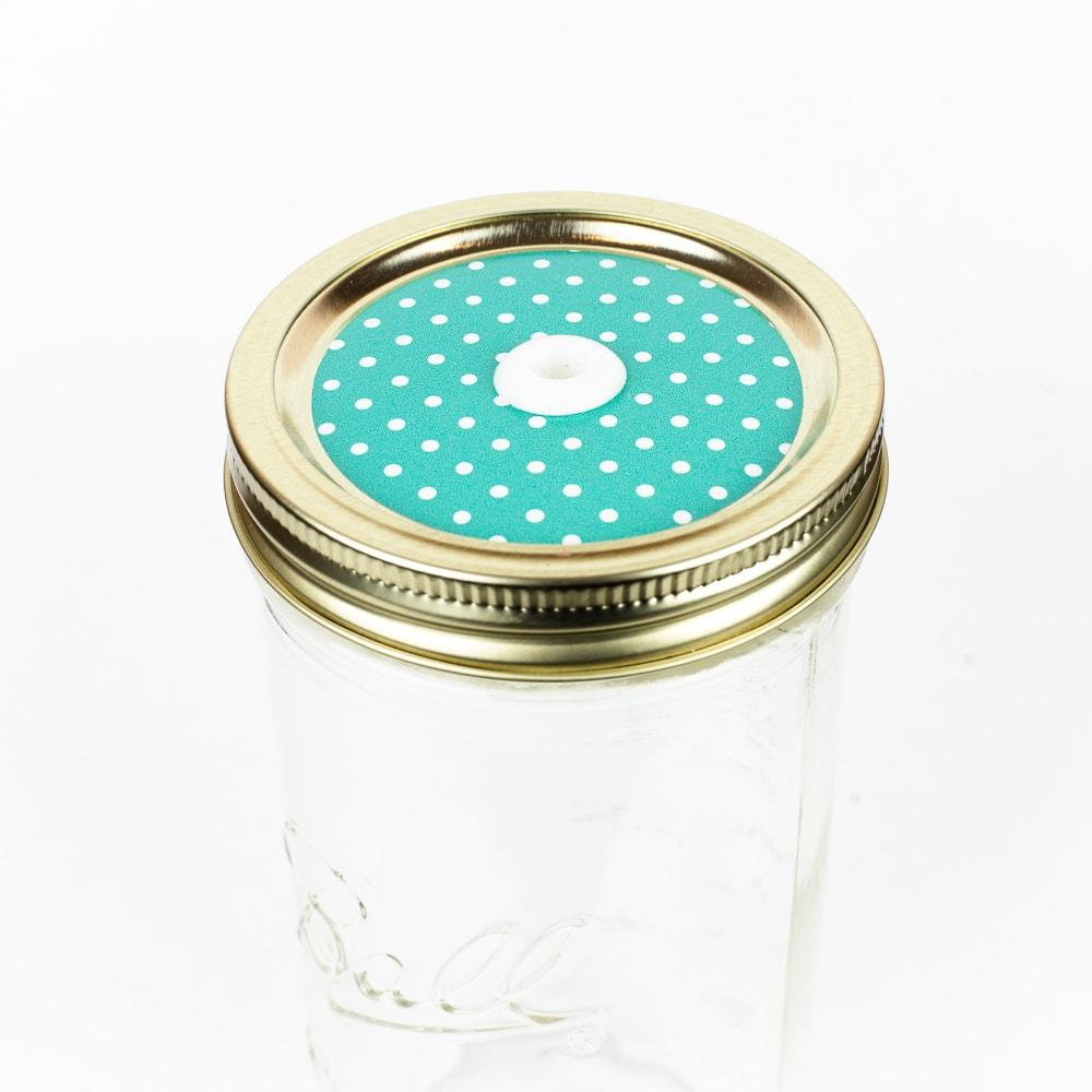 Golden lid with a polka dots on aqua patterned mason jar straw lid against a white background.