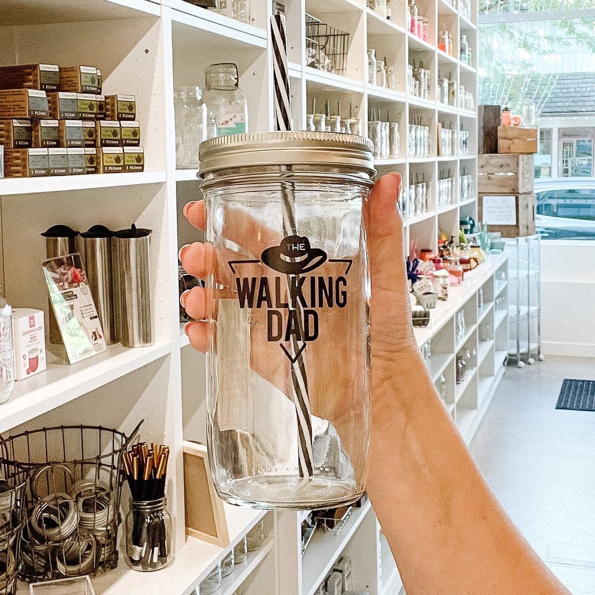 hand holding a mason jar tumbler that says "the walking dad" within a triangle and with a hat above the words