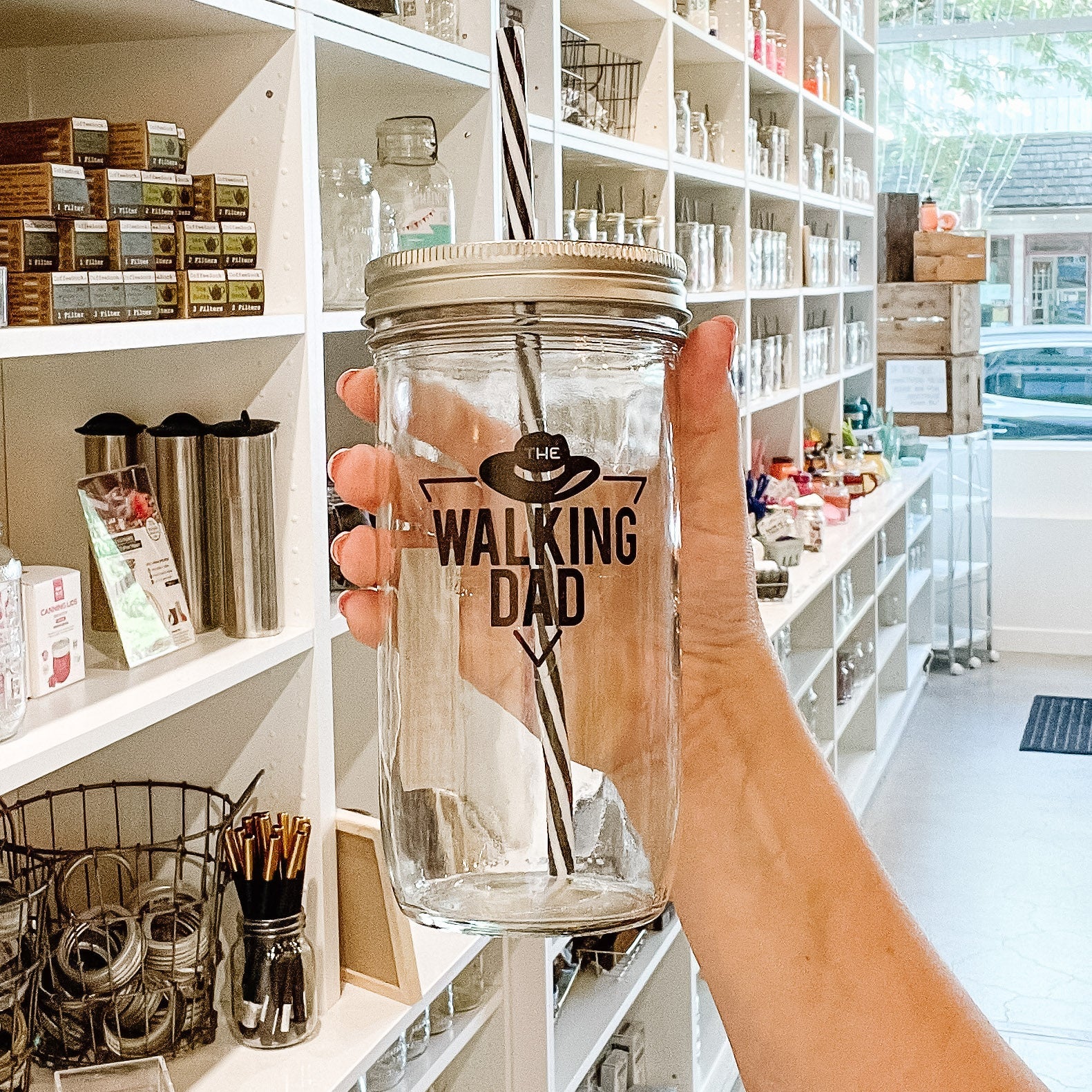 hand holding a mason jar tumbler that says "the walking dad" within a triangle and with a hat above the words
