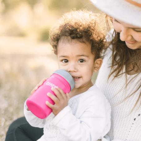 Photo of a child sitting in her mother&#39;s lap drinking from a stainless steel mason bottle with straw top in pink.