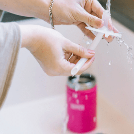 Photo of a woman cleaning the straw of stainless steel mason bottle in pink with running water in a sink.