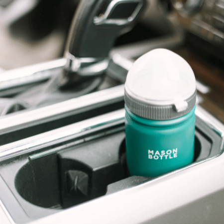 Photo of a stainless steel mason bottle with straw top in forest green placed in a cup holder in a car.